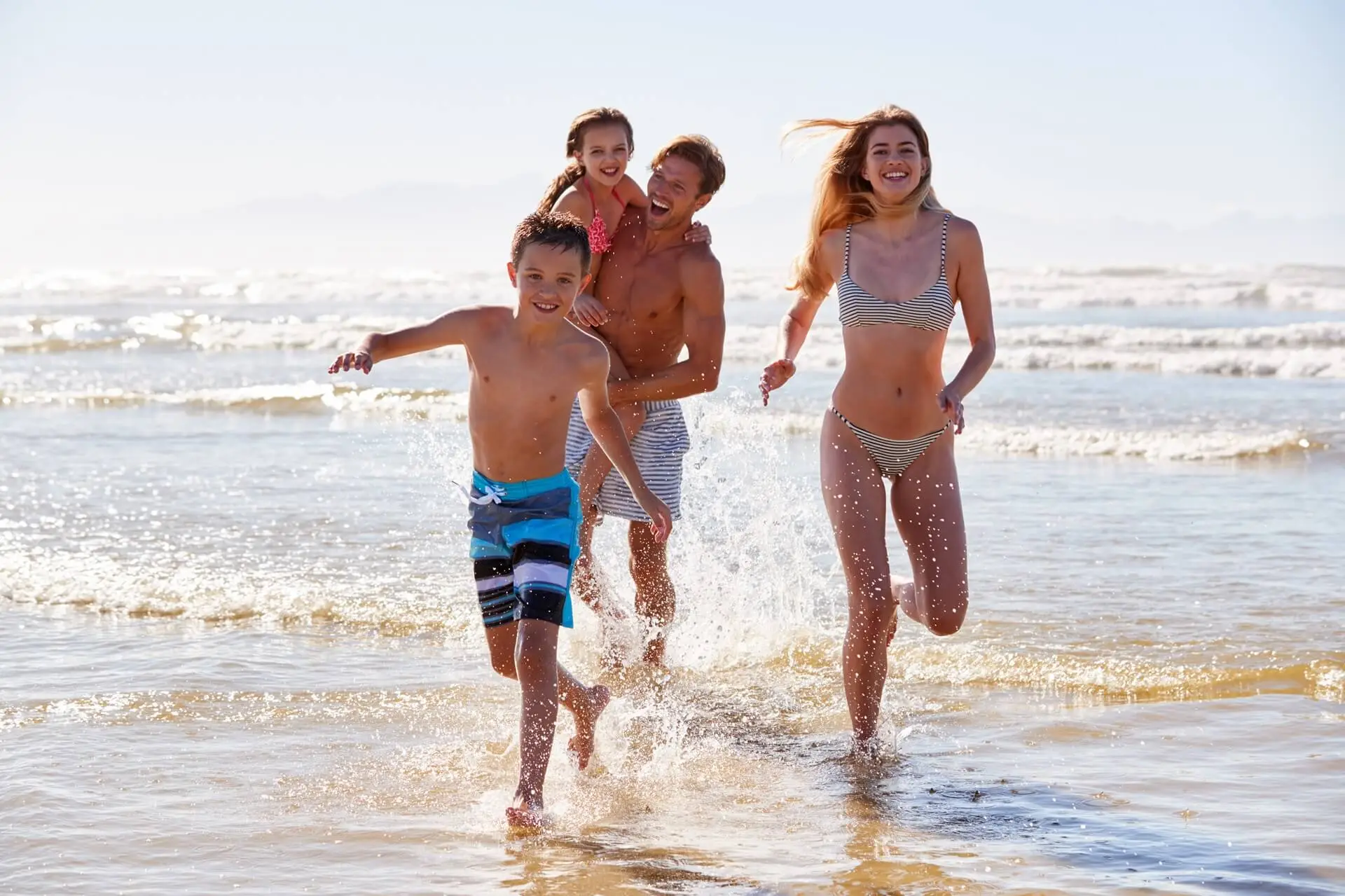 A family joyfully runs through the shallow waves at the beach.