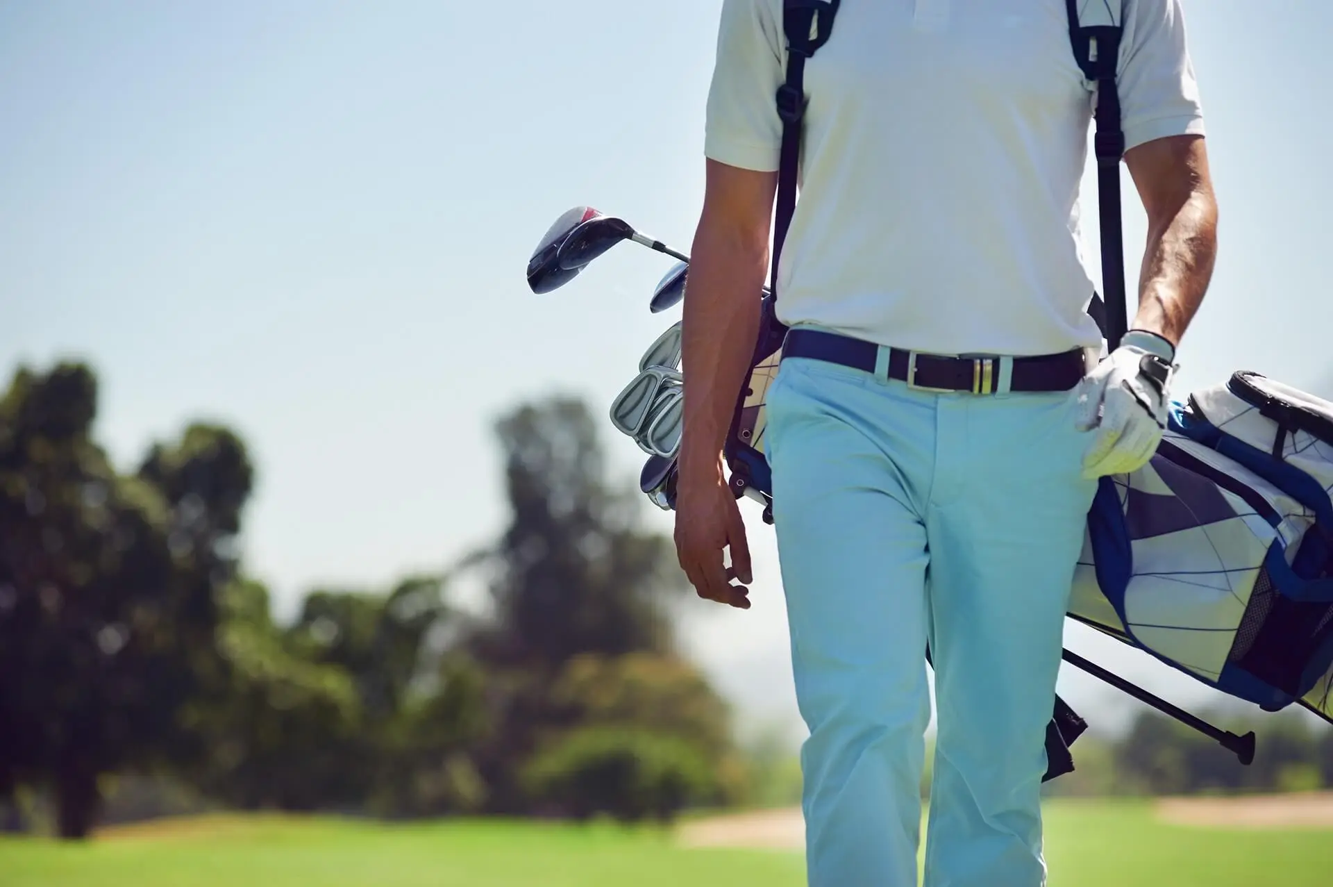 Un golfeur en tenue blanche et bleue marche sur un parcours en portant un sac de clubs.
