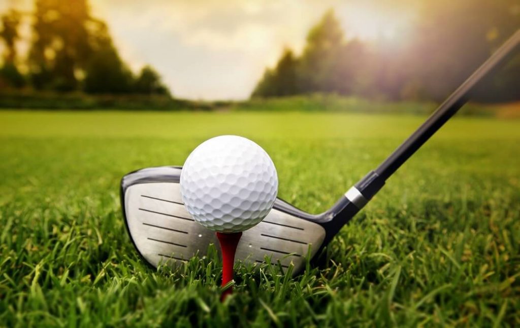 Balle de golf posée sur un tee rouge avec un club prêt à frapper sur le gazon.