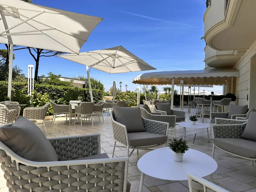 Terrazza esterna con sedie intrecciate, tavolini bianchi e grandi ombrelloni sotto un cielo sereno.