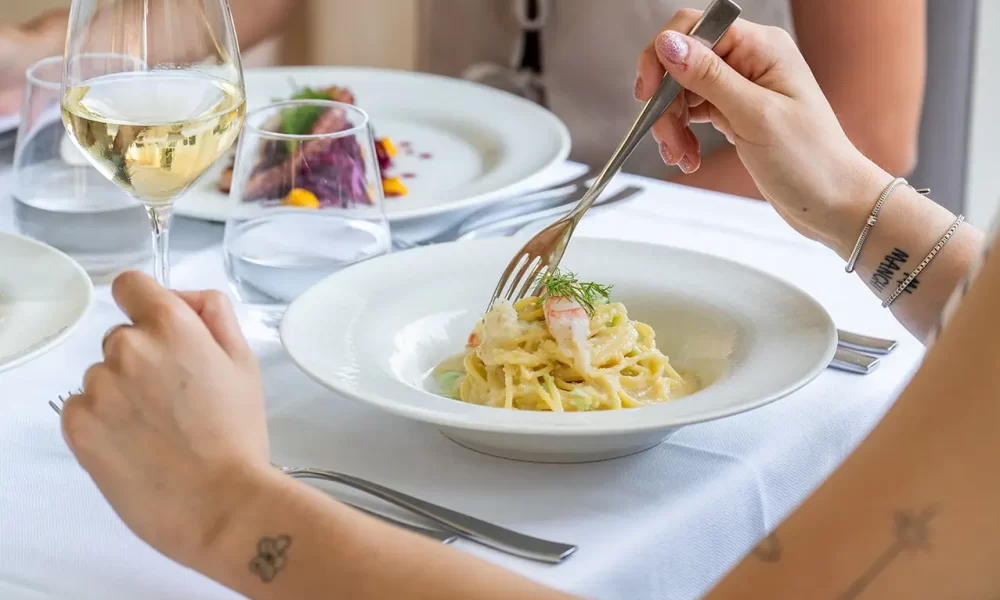 Personnes prenant un repas avec des pâtes et du vin dans un restaurant élégant.