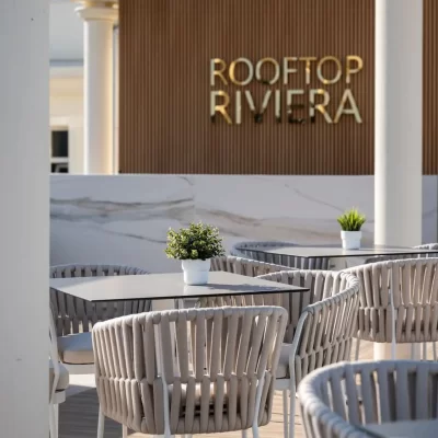 Rooftop seating area with modern chairs and tables, featuring a "Rooftop Riviera" sign.
