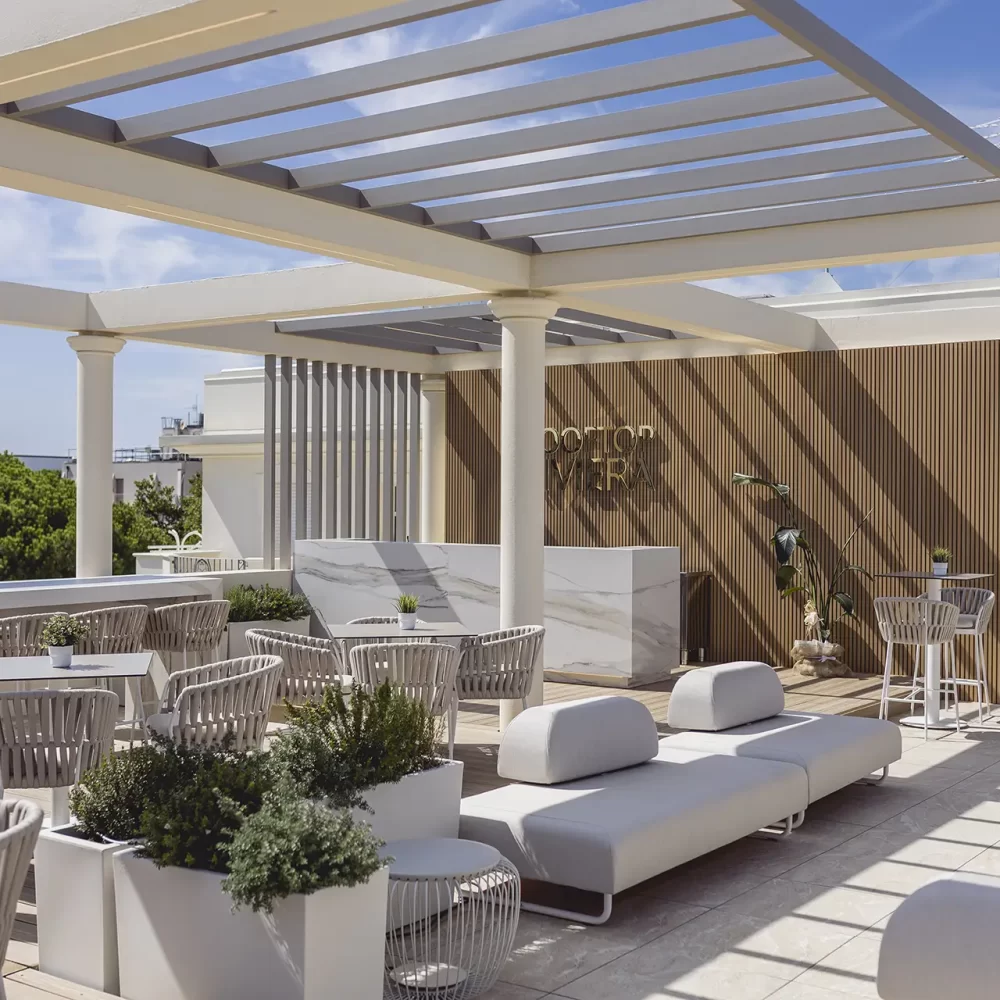 A stylish outdoor rooftop lounge with modern furniture and potted plants under a pergola.