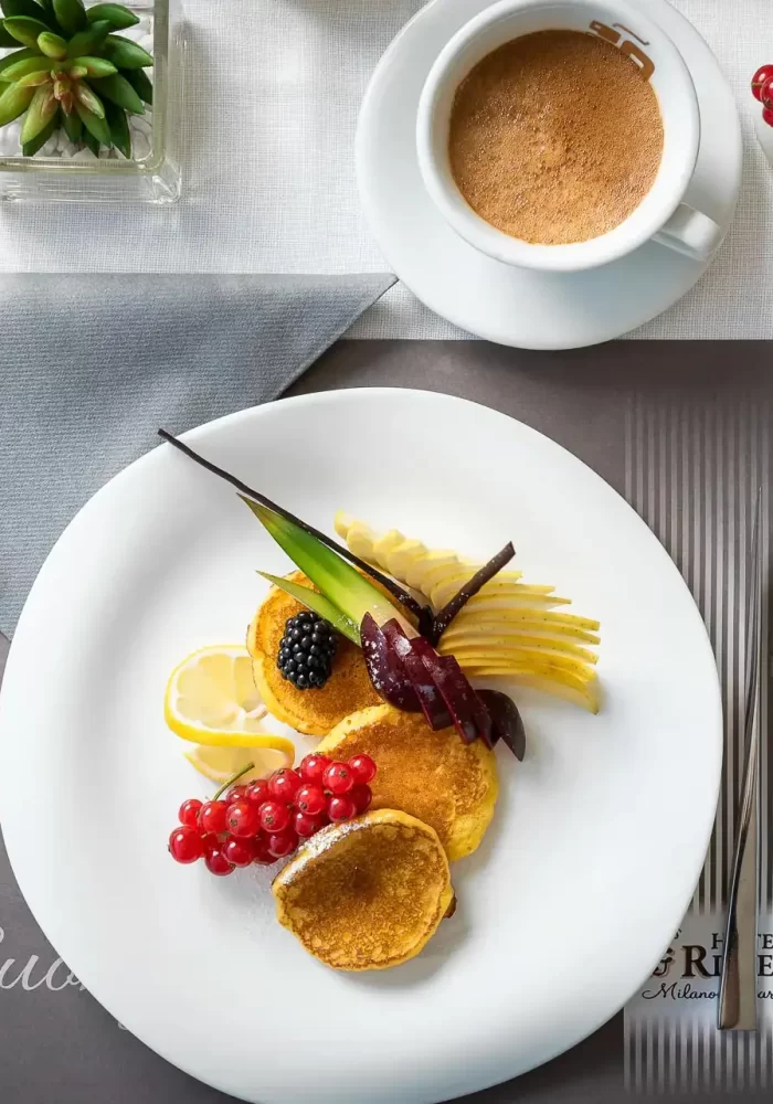 Colazione elegante in hotel con pancake, frutta, croissant e caffè.