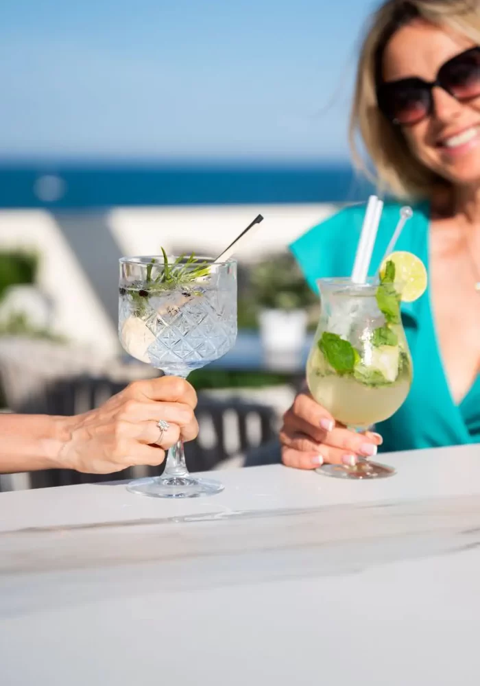 Two people clinking glasses with cocktails by the sea.